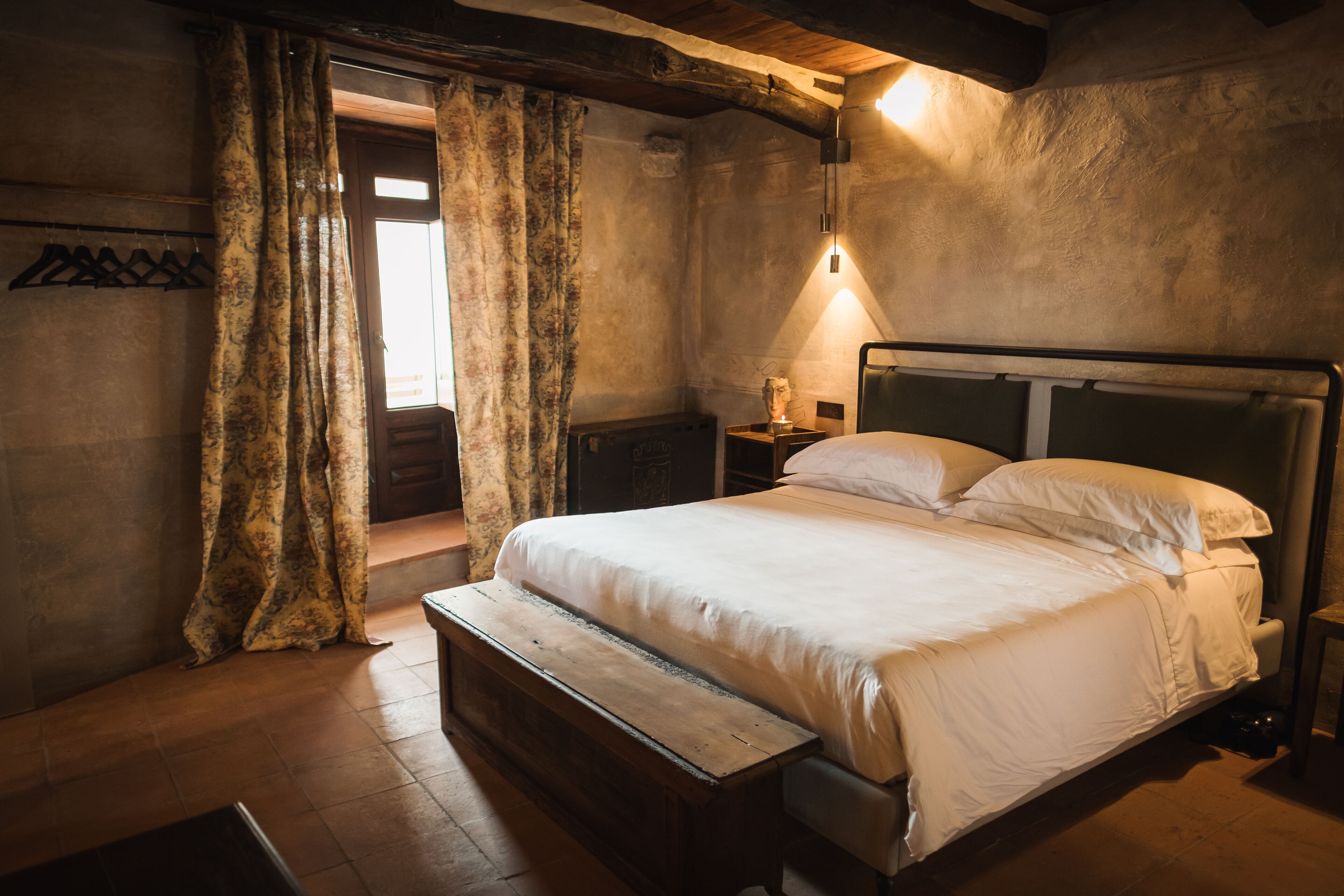 Ein Schlafzimmer mit einem hölzernen Bett, einer Bank, einem Nachttisch und einer Wandlampe.