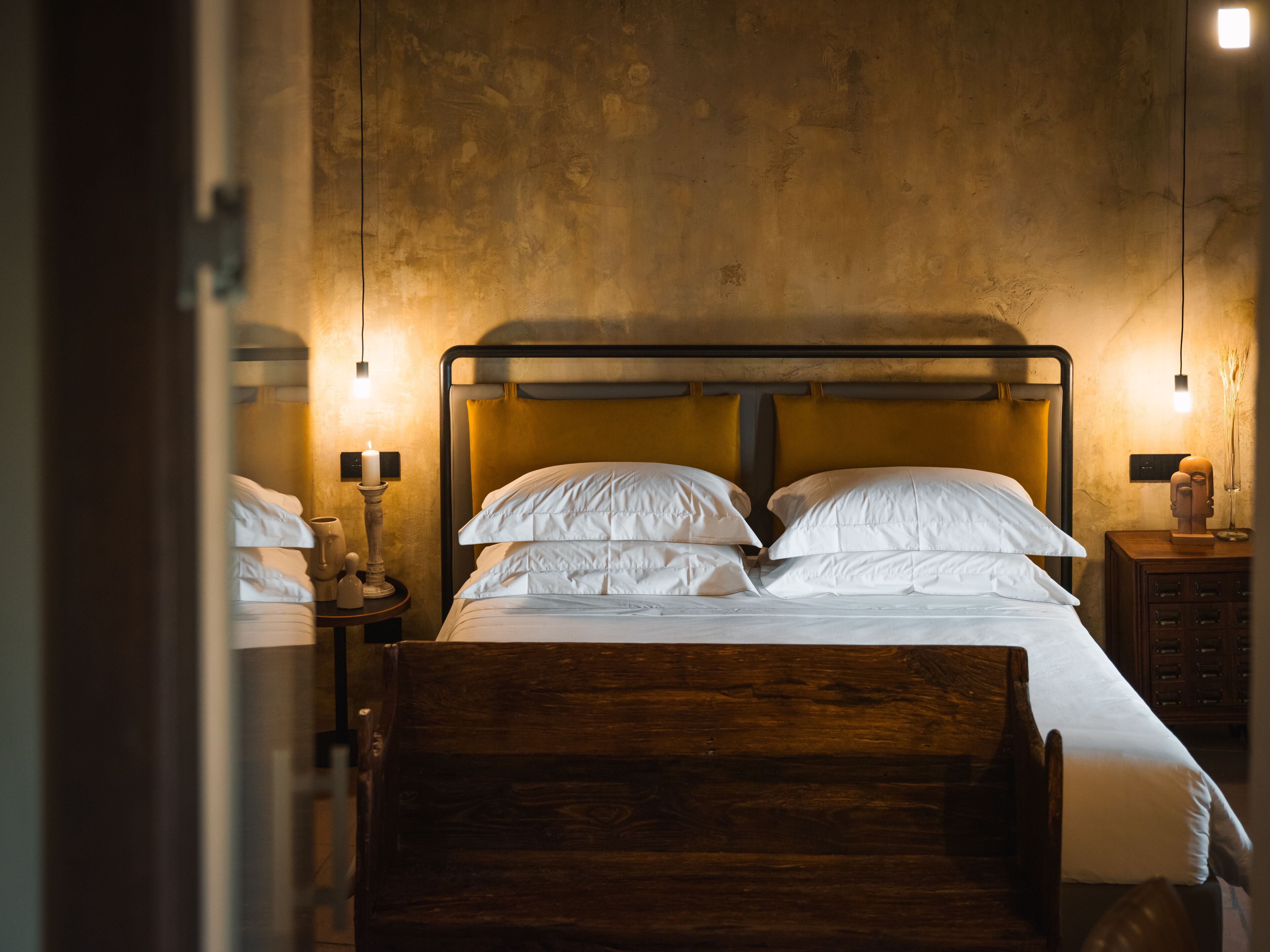 A bedroom with a wooden bed, a bedside table with a lamp, and a wall-mounted light fixture.
