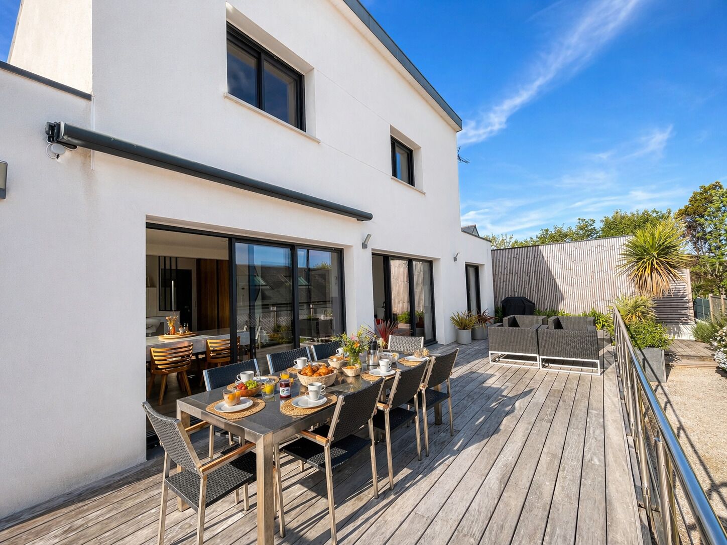 A modern house with a deck, a dining area with a table and chairs, and a barbecue grill.