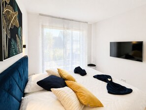 A bedroom with a bed, pillows, a TV, and a window with curtains.