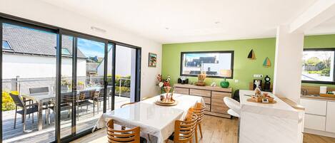 A modern kitchen with a dining area, large windows, and a view of the outdoors.