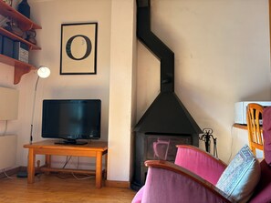 A living room with a television, a fireplace, a wooden table, and a chair.