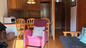 Une cuisine compacte dotée de meubles en bois, d’un four à micro-ondes et d’un réfrigérateur. On y trouve un coin repas avec une table et des chaises en bois, ainsi qu’un canapé dans l’espace de vie.