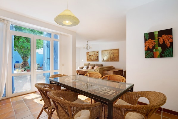 A dining area with wicker chairs, a glass table, and a chandelier.