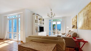 A room with a bed, a sofa, a bookshelf, a TV, and a large window. - Vacation Home "Villa Lucila" with Sea View, Garden & Wi-Fi (Corralejo)
