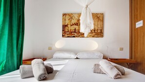 A hotel room with a bed, pillows, a bedside table, a lamp, a painting on the wall, and a green curtain. - Vacation Home "Villa Lucila" with Sea View, Garden & Wi-Fi (Corralejo)