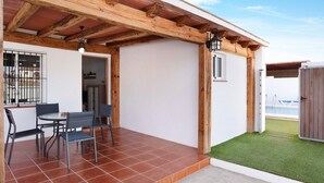 Un patio exterior con una pérgola de madera, una mesa de comedor con sillas y vistas a una piscina.
