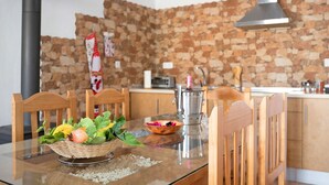 Una mesa de comedor con cubierta de vidrio, rodeada de sillas de madera, en una cocina con pared de piedra y electrodomésticos modernos.