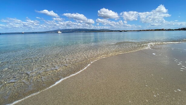 A beach with clear water, a boat, and distant land. - Holiday Home "Samarighouse" close to the Sea with Garden & Wi-Fi (Sa Rocca Tunda)