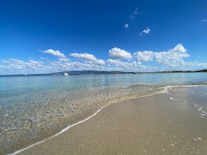 A beach with clear water, a boat, and distant land.