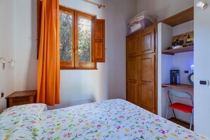 A bedroom with a bed, a window with curtains, wooden cabinets, and a chair.