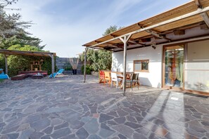 A patio with stone flooring, a wooden pergola, and a dining area with chairs and a table.