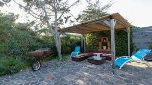 An outdoor patio with stone flooring, a wooden pergola, wicker furniture, and a wheelbarrow. - Holiday Home "Samarighouse" close to the Sea with Garden & Wi-Fi (Sa Rocca Tunda)