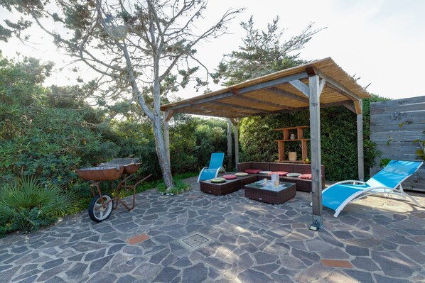 An outdoor patio with stone flooring, a wooden pergola, wicker furniture, and a wheelbarrow.
