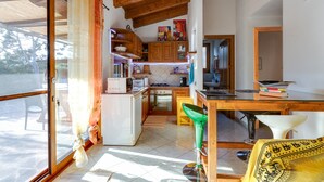 A kitchen with wooden cabinets, a refrigerator, a stove, and a dining area with a table and chairs. - Holiday Home "Samarighouse" close to the Sea with Garden & Wi-Fi (Sa Rocca Tunda)
