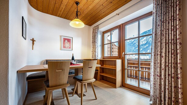 A room with a wooden desk, two chairs, a hanging light fixture, a window with a view of mountains, and a wooden shelf. - Apartment "Duregger App Sonnenschein" with Mountain View, Garden & Wi-Fi (Sand in Taufers)