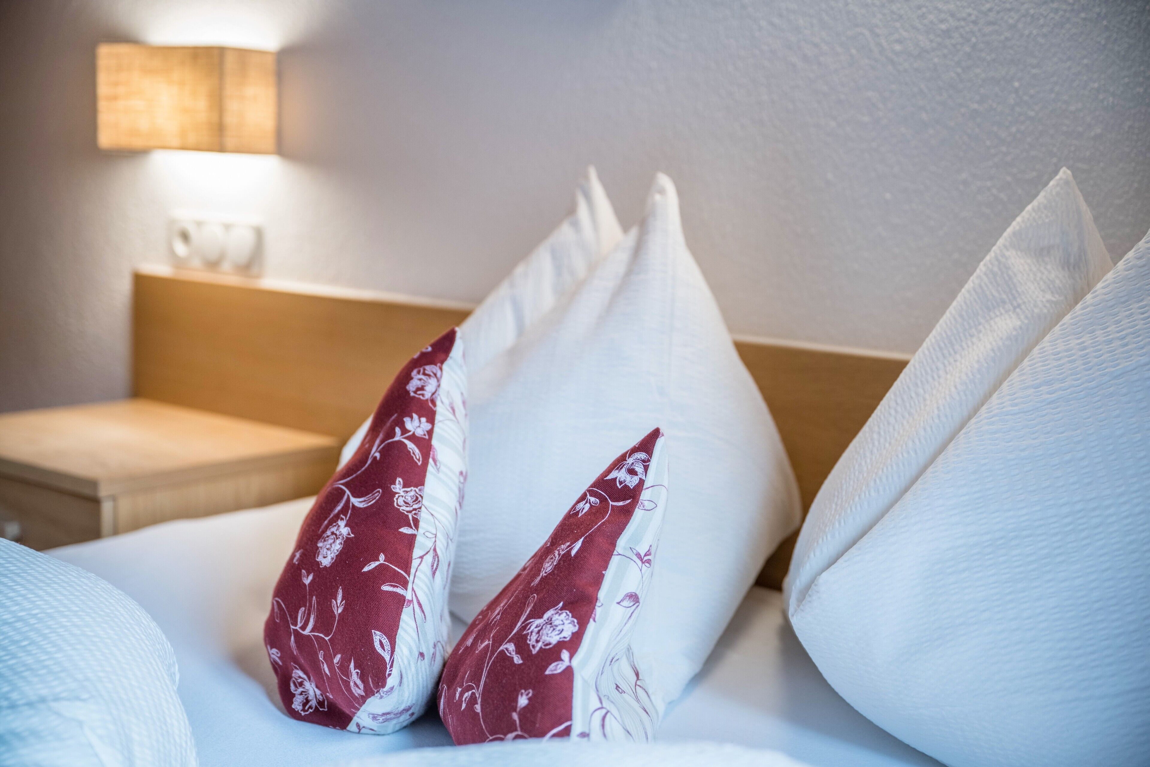 Una camera d'albergo con un letto, cuscini, un comodino e una lampada a parete.