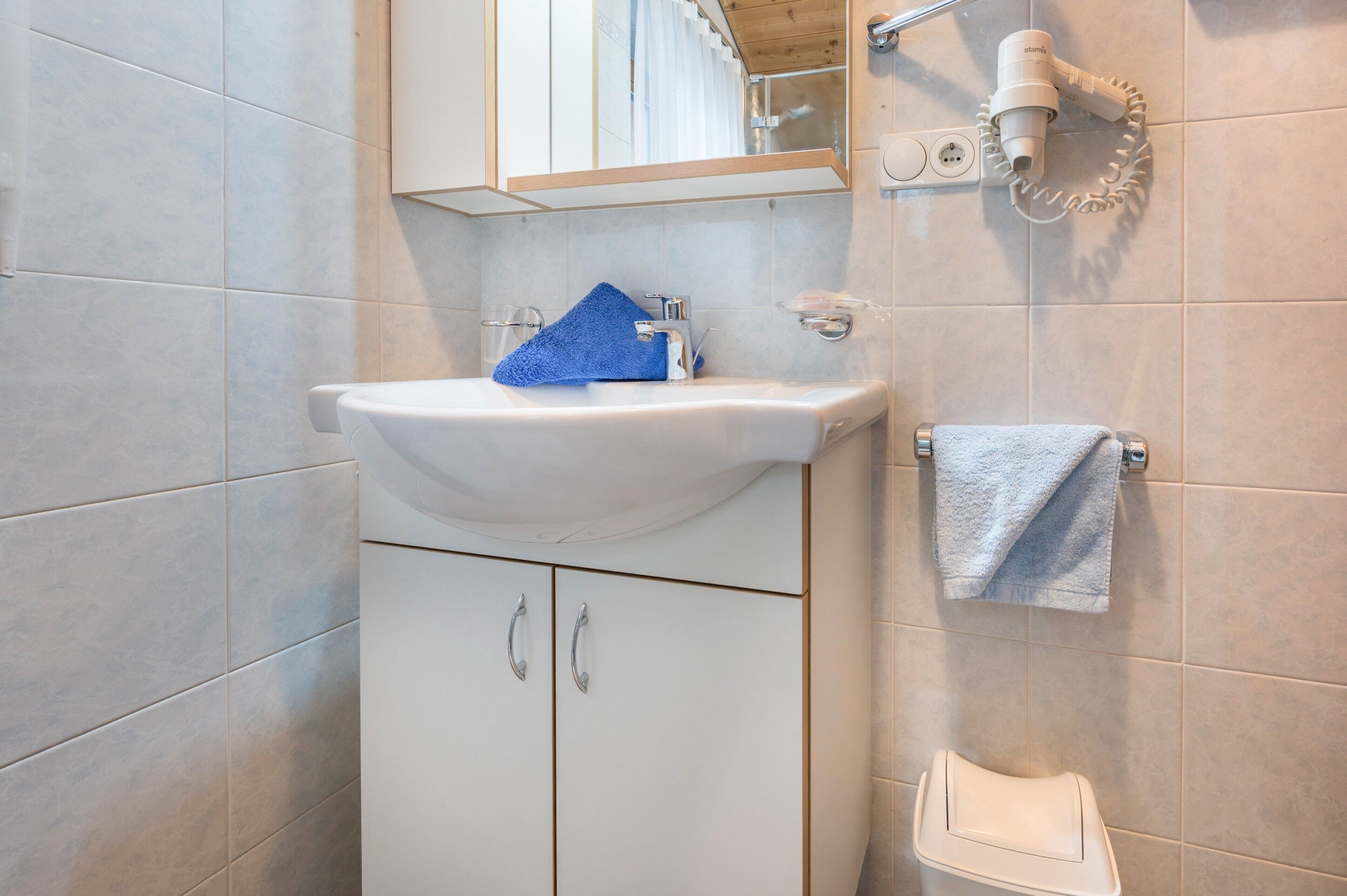 Een badkamer met een witte wastafel, een handdoekhouder en een haardroger bevestigd aan de muur.
