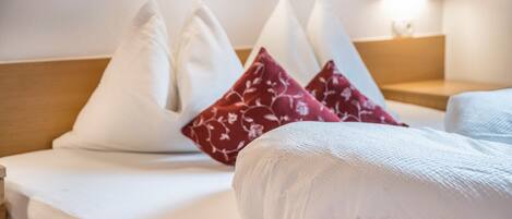 Ein Hotelzimmer mit einem ordentlich bezogenen Bett, Kissen in Weiß und Rot mit Muster, einem Holzkopfstück und einer Nachttischlampe.