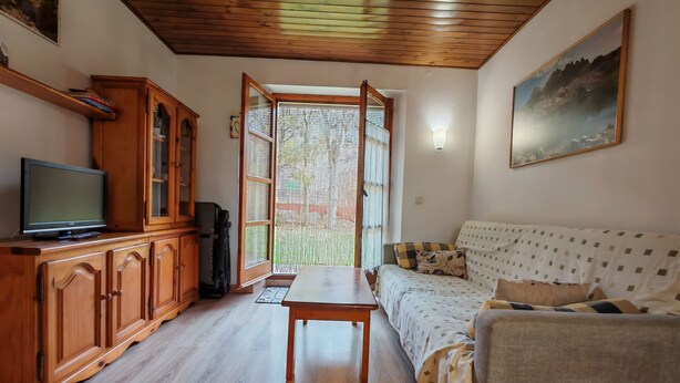 Een woonkamer met een tv-meubel van hout, een bank, een eettafel en een groot raam met uitzicht.
