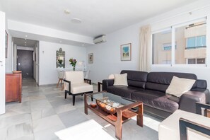 A modern living room with a leather sofa, a glass coffee table, and a white armchair.