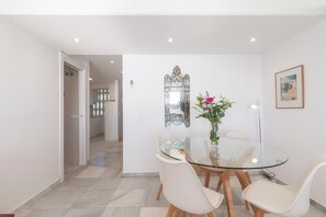 A dining area with a glass table, white chairs, a decorative mirror, and a vase with flowers.