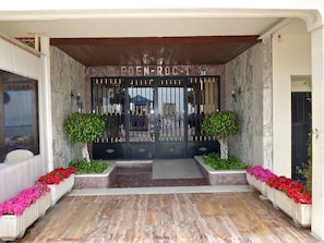 L’entrée d’un hôtel, avec une façade en marbre, un portail en métal et des jardinières.