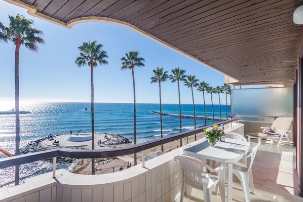 A balcony with a view of the ocean, palm trees, and a beach area.