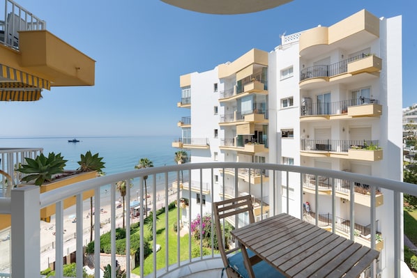 A balcony with a view of the sea, a wooden table, and a white railing.