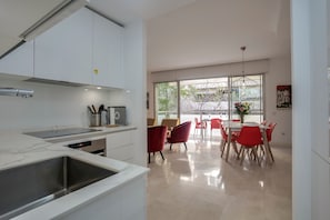 A modern kitchen with a built-in oven, a stainless steel sink, and a dining area with red chairs and a table.