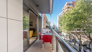 Un balcón con puerta de cristal, sillas rojas y una mesa cubierta con mantel blanco.