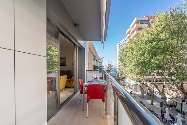 A balcony with a glass door, red chairs, and a table with a white tablecloth.