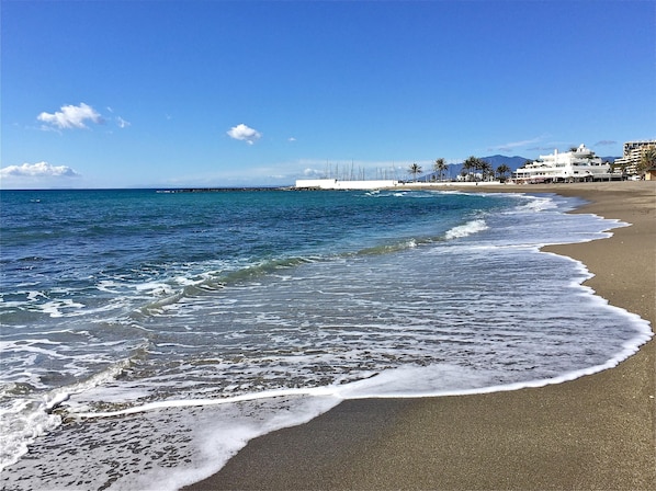 A beach with waves, a pier, and buildings in the background.