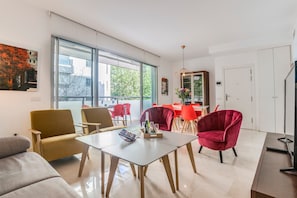 A modern living room with a large window, a dining area with red chairs, and a sofa.