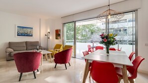 Una sala de estar moderna con un sofá, sillas rojas, una mesa de comedor y ventanas grandes.