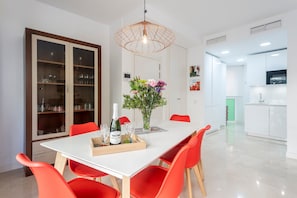 A modern dining area with a white table, red chairs, a glass cabinet, and a pendant light.