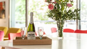 Una botella de champán Brut en una bandeja con dos copas, un florero y una mesa en una habitación luminosa con ventanas amplias.