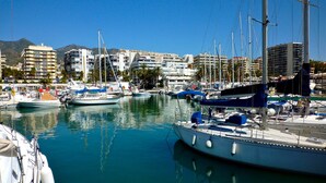 Un puerto deportivo con barcos amarrados, cielo despejado y edificios al fondo.