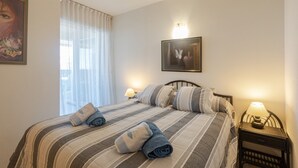 A bedroom with a bed, pillows, a nightstand with a lamp, a framed picture on the wall, and a window with curtains. - Apartment with Shared Pool, Sea View, Wi-Fi and Air Conditioning (Marbella)