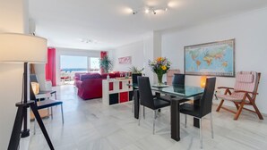 A modern living room with a glass dining table, black chairs, a red sofa, and a world map on the wall. - Superb Spacious Seafront Apartment with Sea View, Wi-Fi, and Air Conditioning (Marbella)