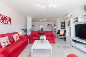 Una sala de estar con un sofá rojo, una mesa de centro blanca y un televisor de pantalla plana.