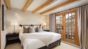 Ein Schlafzimmer mit Bett, Nachttischen, Lampen, einem Fenster mit Vorhängen und einer Holzbalkendecke.