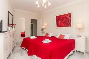 Un dormitorio con dos camas, un espejo, un cuadro de una rosa roja y un armario blanco.