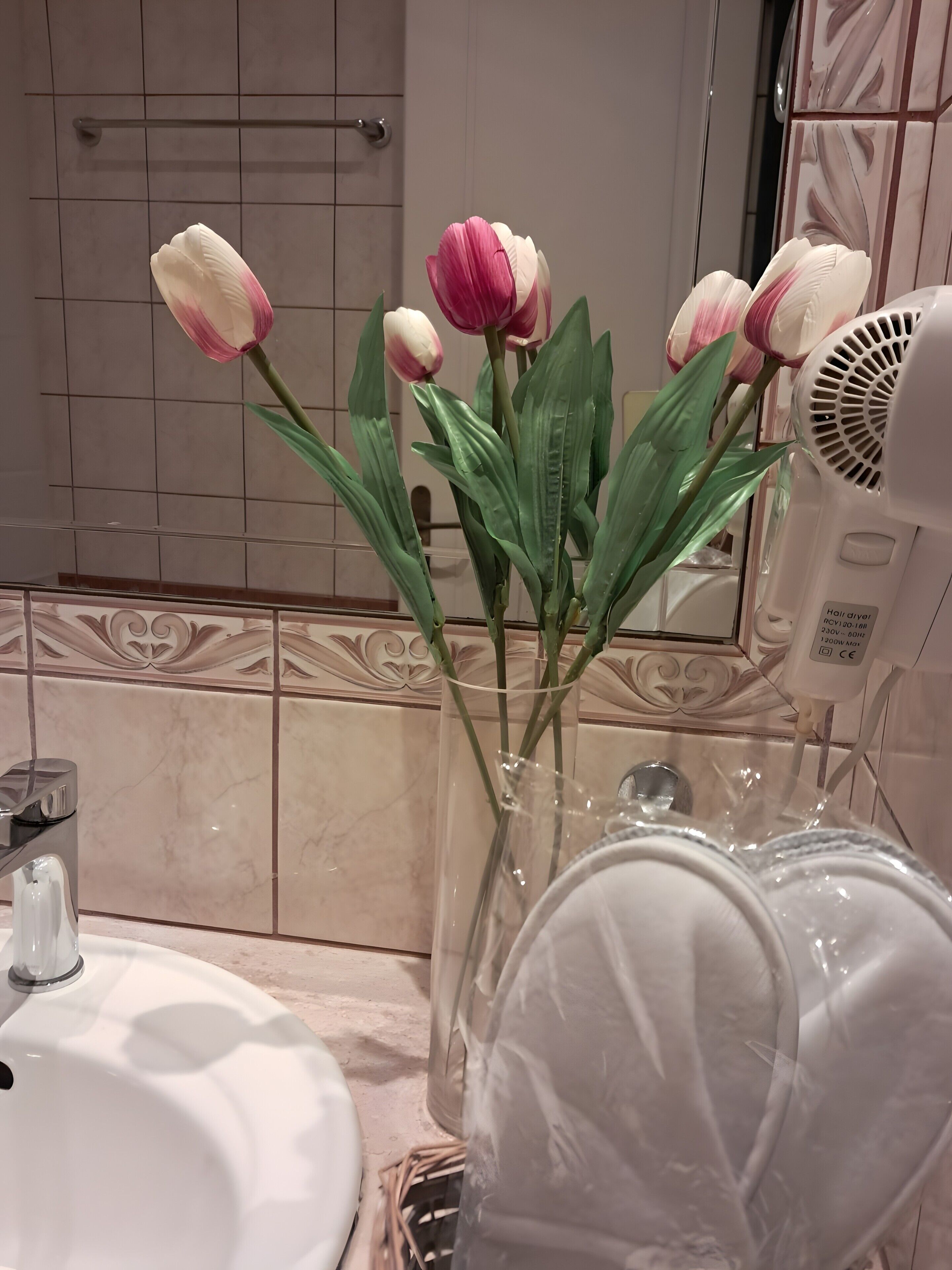 A bathroom with a sink, mirror, and a vase with flowers.