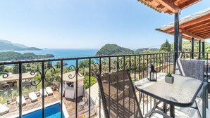 A balcony with a view of the sea, a pool, and lounge chairs.