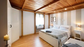 Une chambre avec un plafond en bois, un lit recouvert d’une couvre-lit à motifs, une table de chevet et une commode, ainsi qu’une horloge fixée au mur.