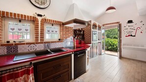 Une cuisine avec un plan de travail rouge, un lave-vaisselle et une fenêtre ornée de rideaux à motifs de cœurs.
