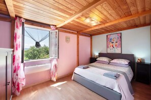Une chambre à coucher avec un lit, une fenêtre avec des rideaux, un tableau au mur et un ventilateur de plafond.