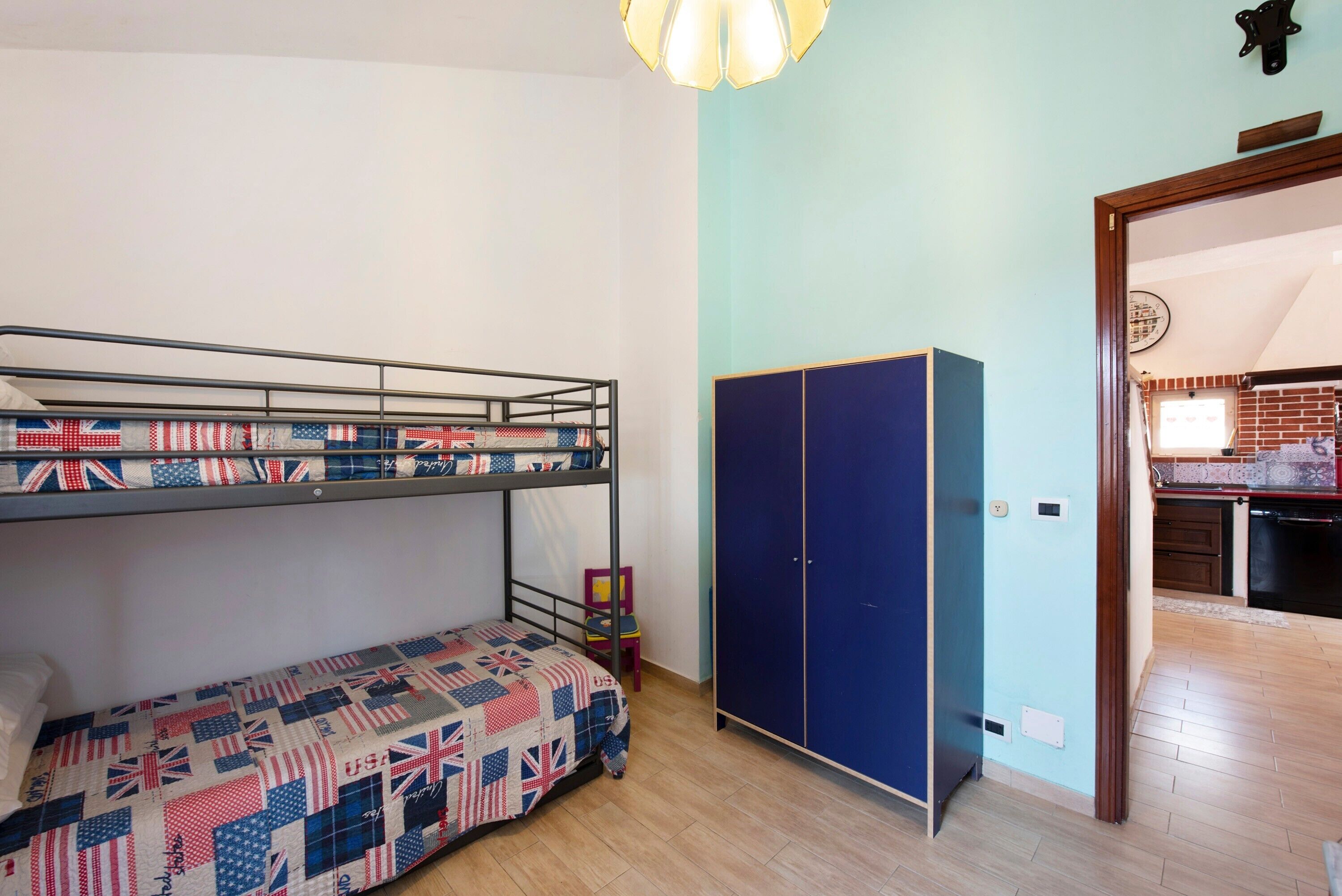 A bunk bed with a quilt, a wardrobe, and a kitchen area in the background.