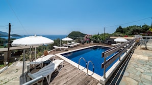 Una piscina con cubierta de madera, sillas de descanso y sombrillas.